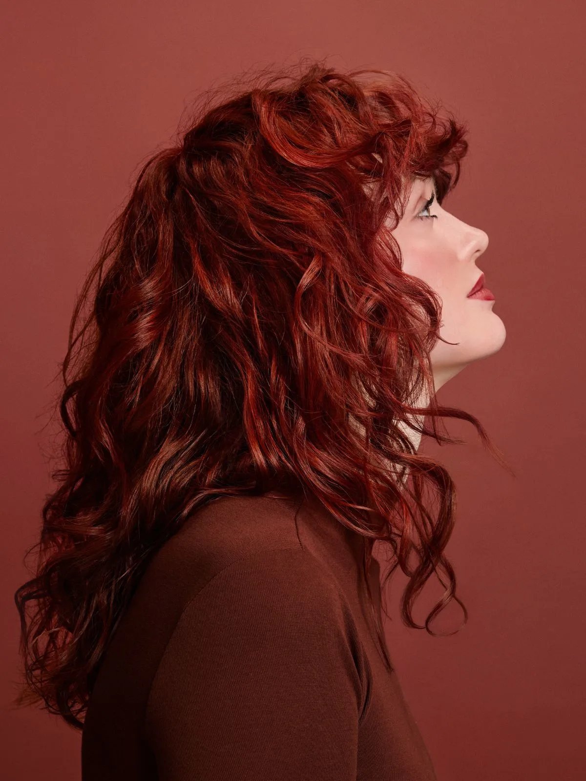 Model with rich copper red curls, wearing a red leather jacket against a red backdrop.
