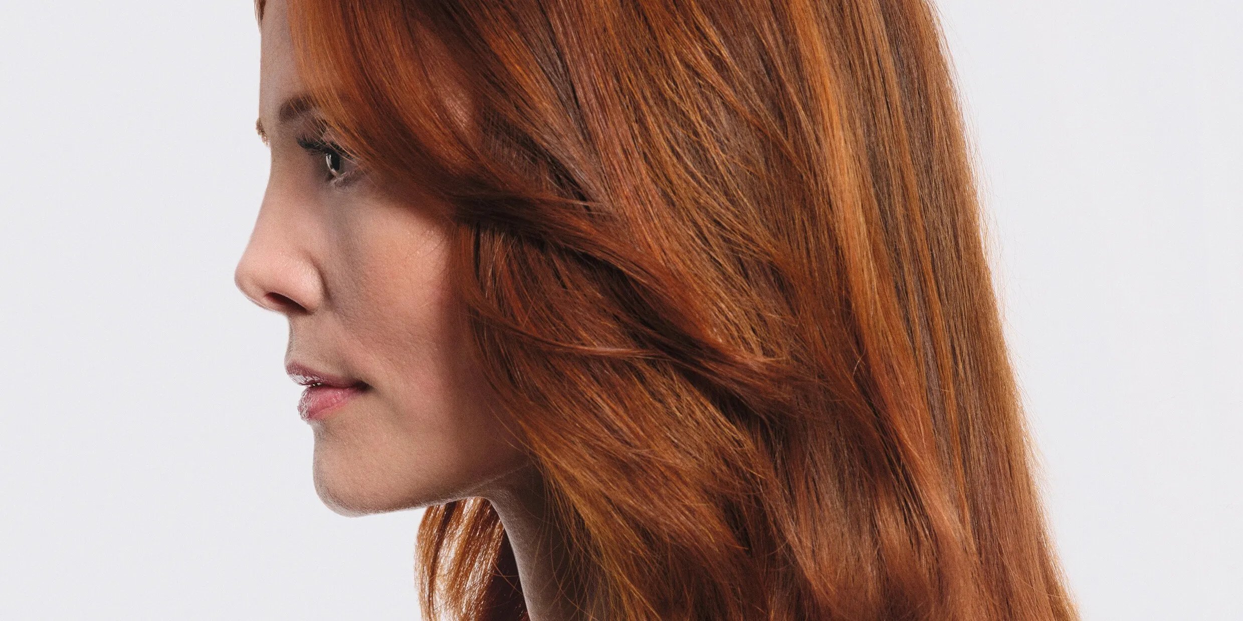 Model with long, loosely curled, copper hair with a honey blonde glow.