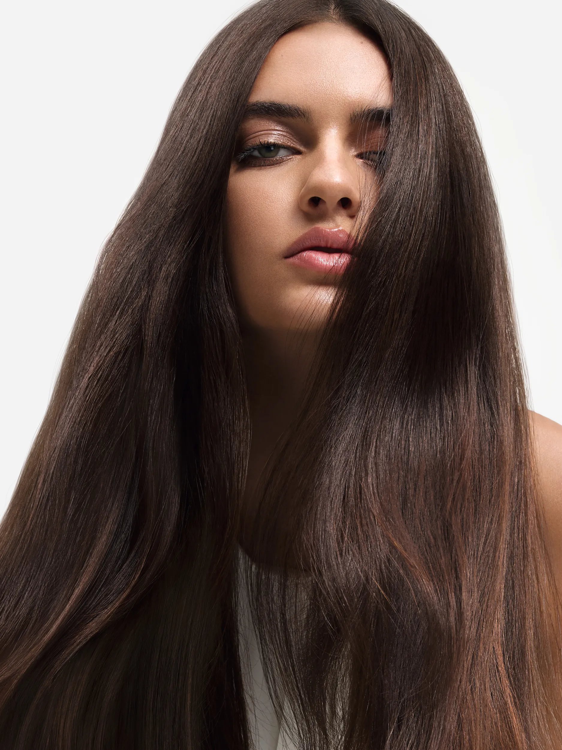 Image of model with long brunette hair slightly covering their face. 
