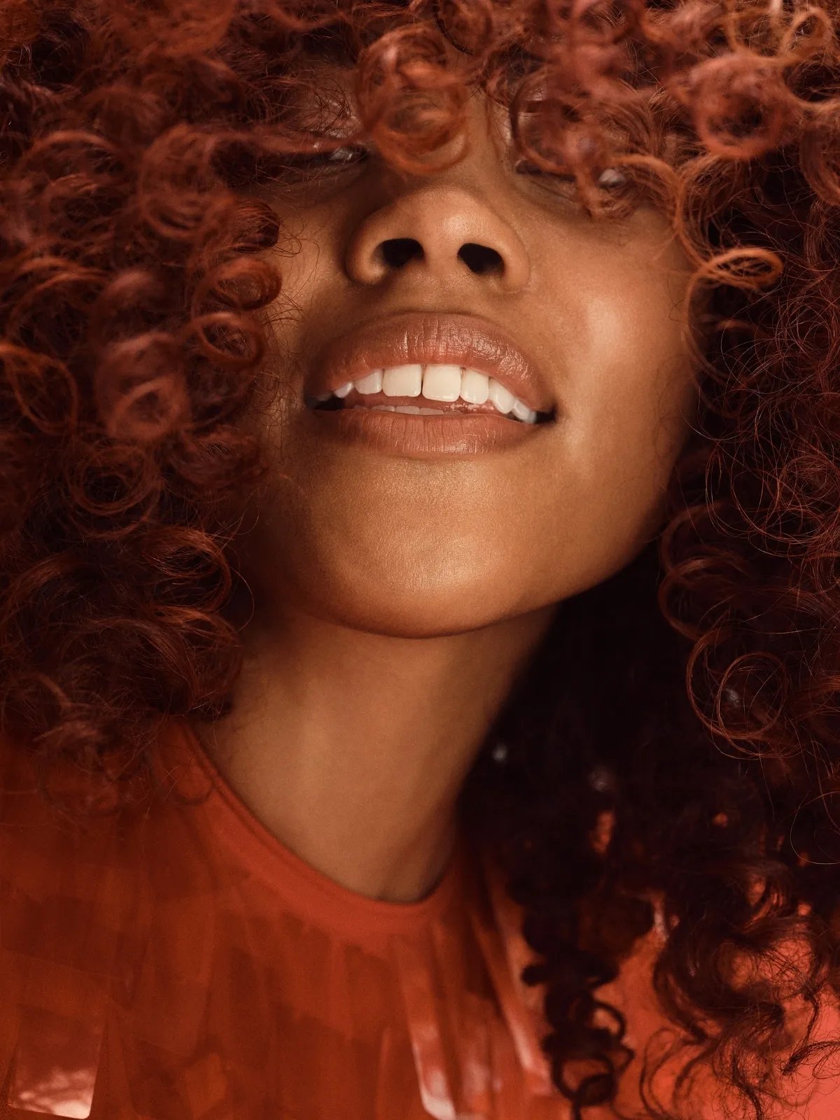 Model’s cinnamon brown, curly hair covers their eyes.