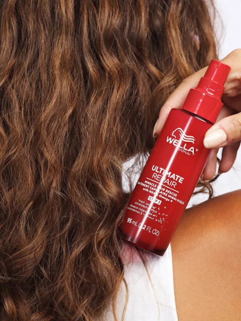 Model with light brown, wavy hair holds ULTIMATE REPAIR Miracle Hair Rescue.