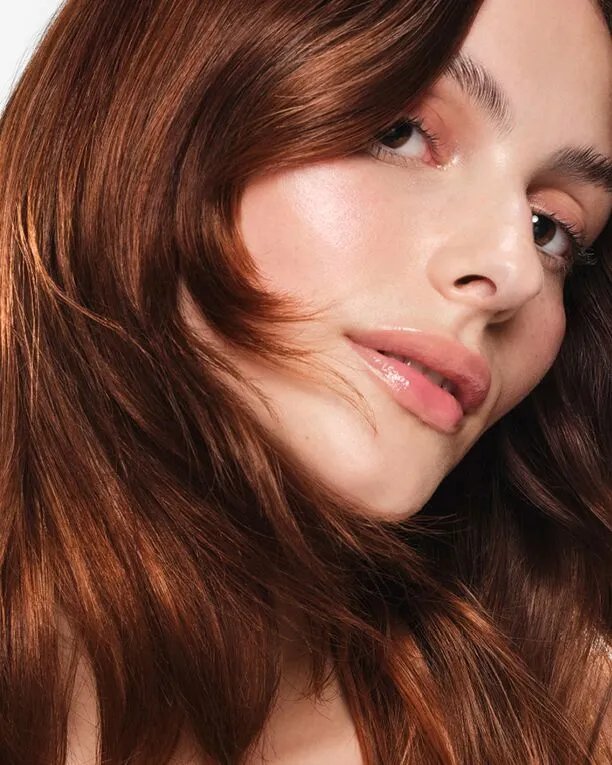 Close-up of a woman with shoulder-length, auburn hair styled with face-framing layers.