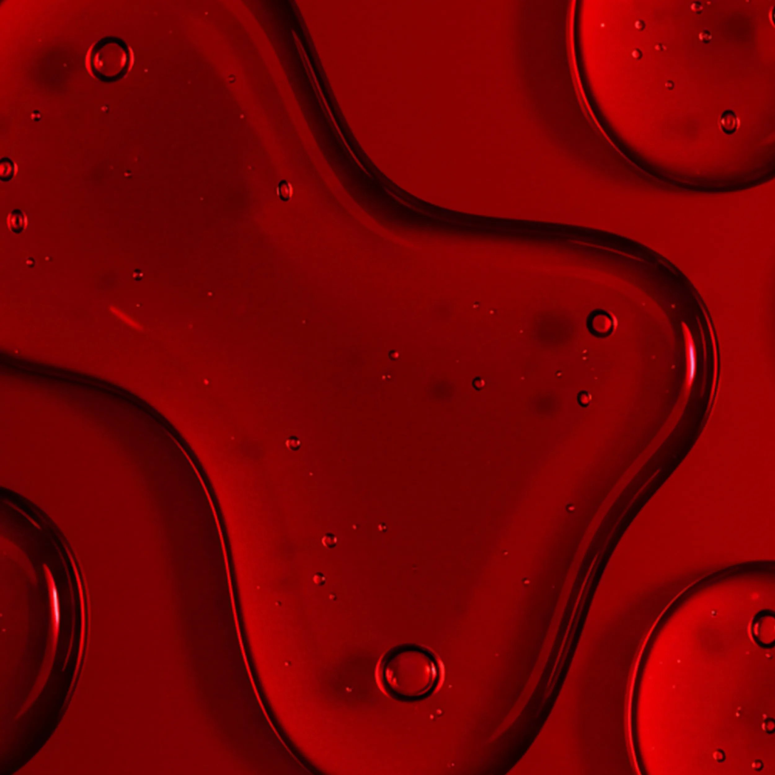 Close-up of clear red liquid droplets and a smear on a textured red surface.