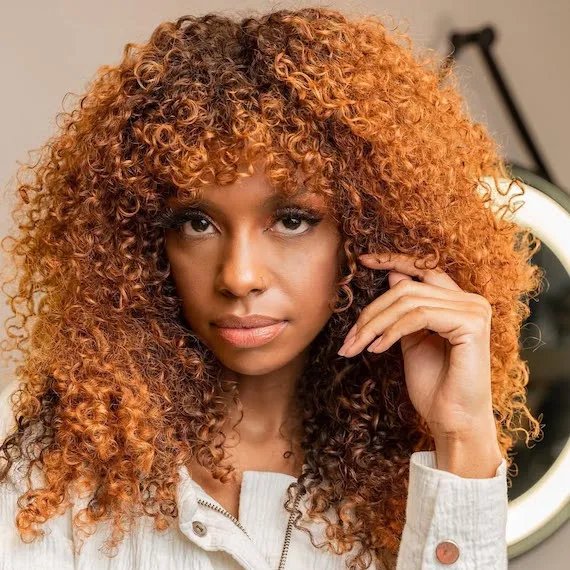 Model with dark brown curly hair featuring a copper peach shade through the lengths.