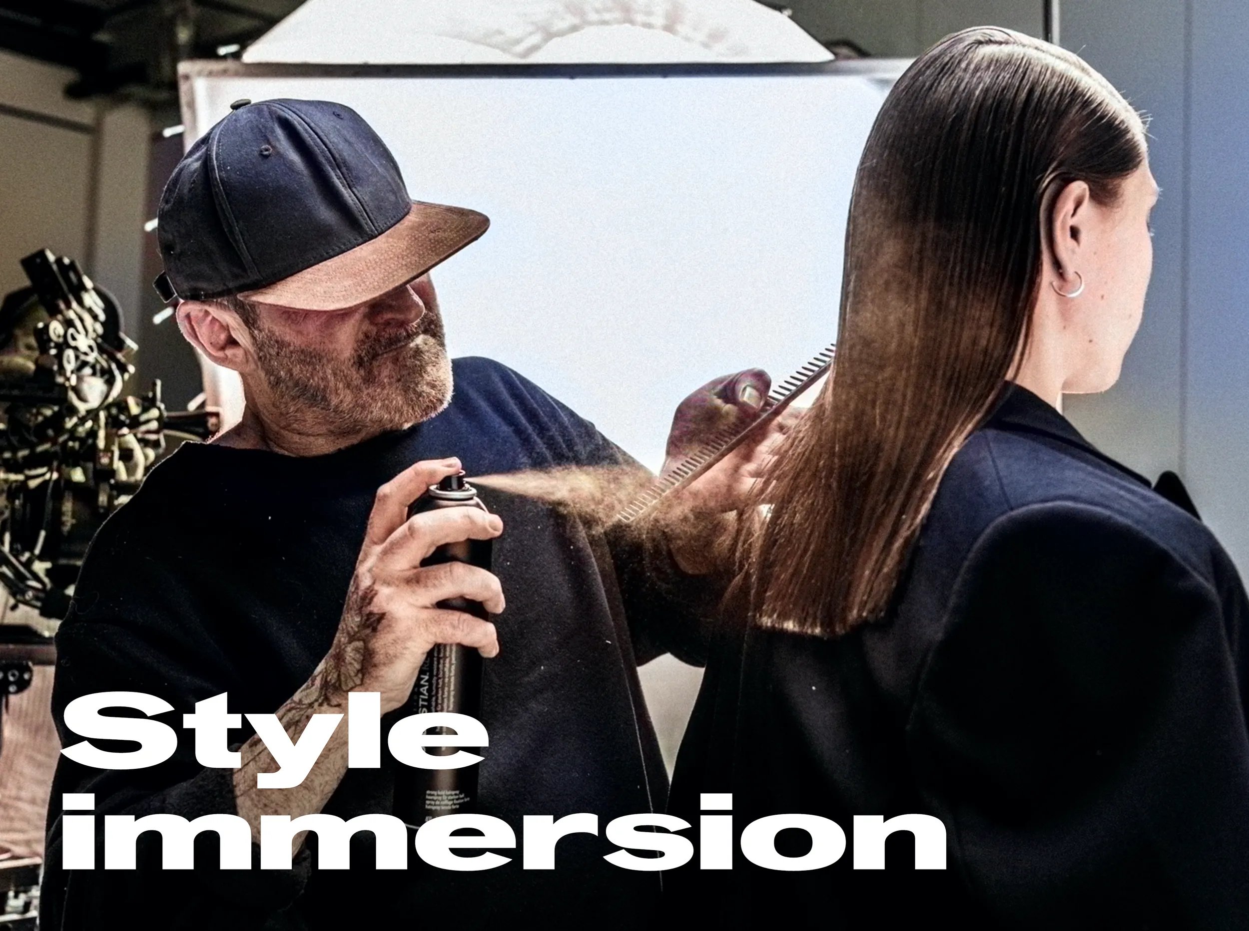 Immagine di un parrucchiere che indossa un cappello e spruzza la lacca sui capelli di una modella girata di spalle. 