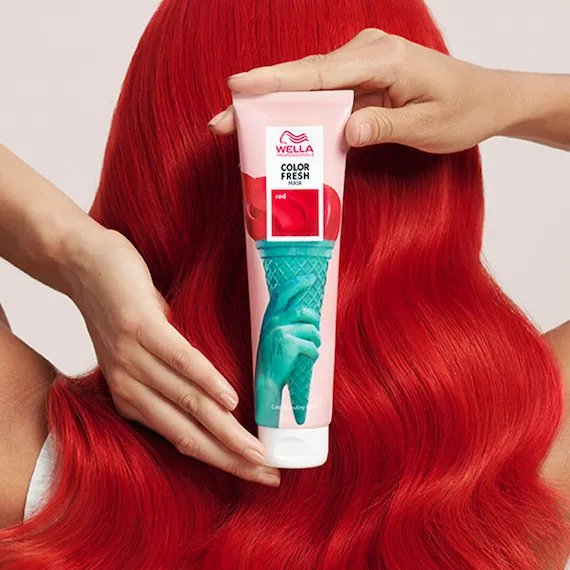 Back of woman’s head showing red, wavy hair and hands holding a tube of the Color Fresh Mask in Red.