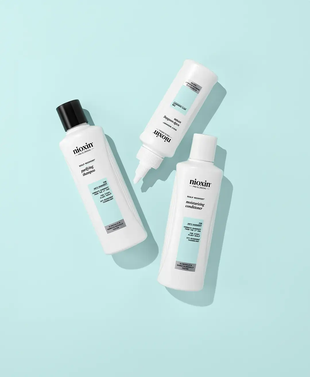 nioxin shampoo, conditioner and scalp soothing serum bottles against baby blue background