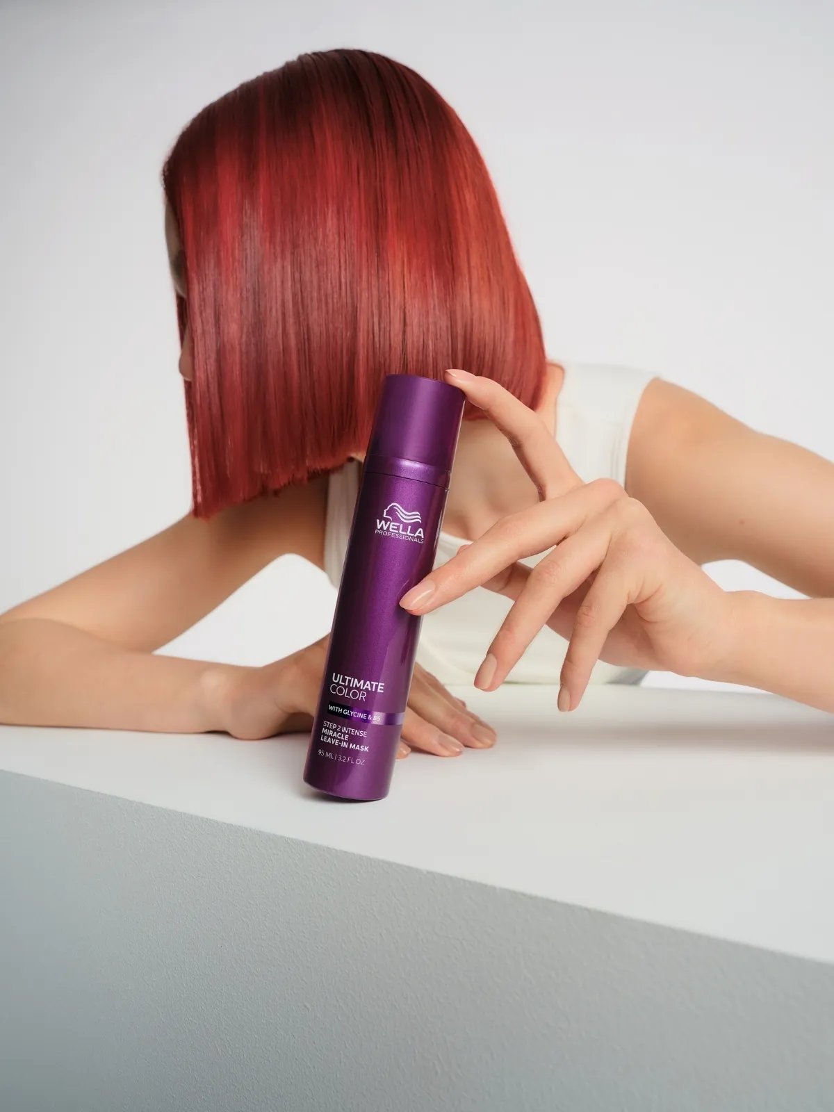 Model with bright red bob haircut holds a bottle of ULTIMATE COLOR Miracle Leave-In Mask.