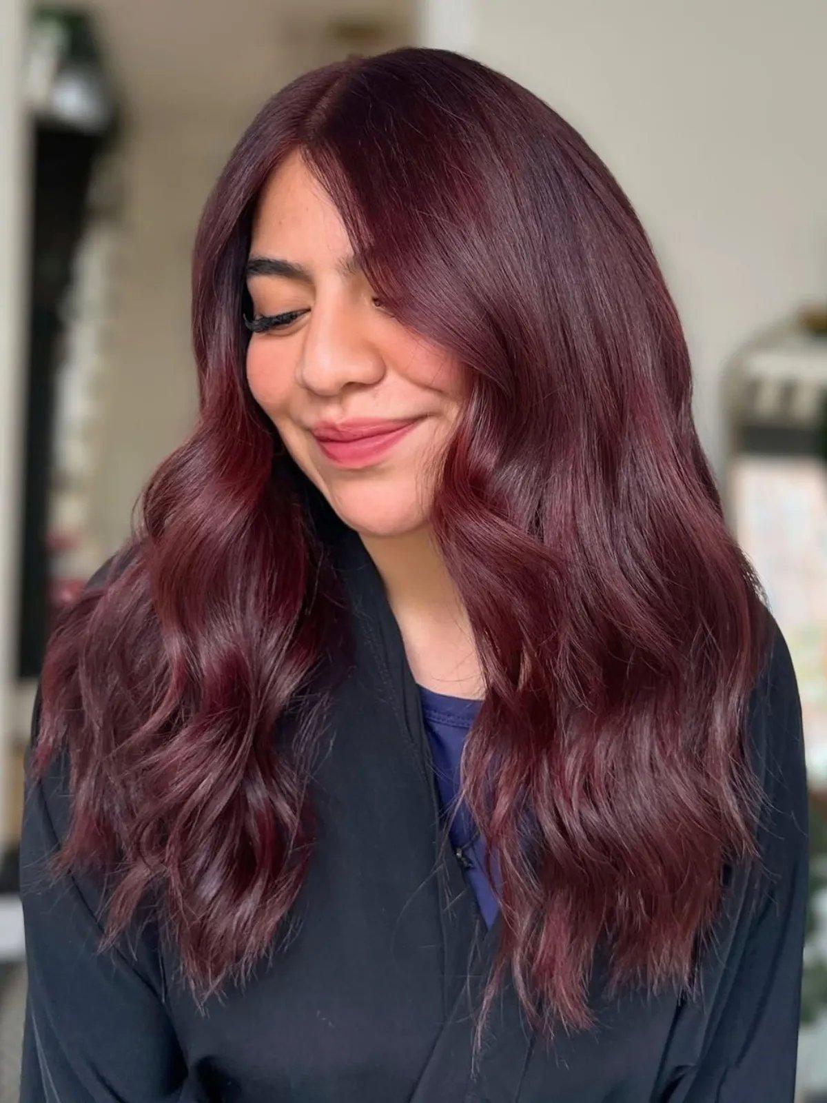 Model with wavy, cool-toned maroon red hair.
