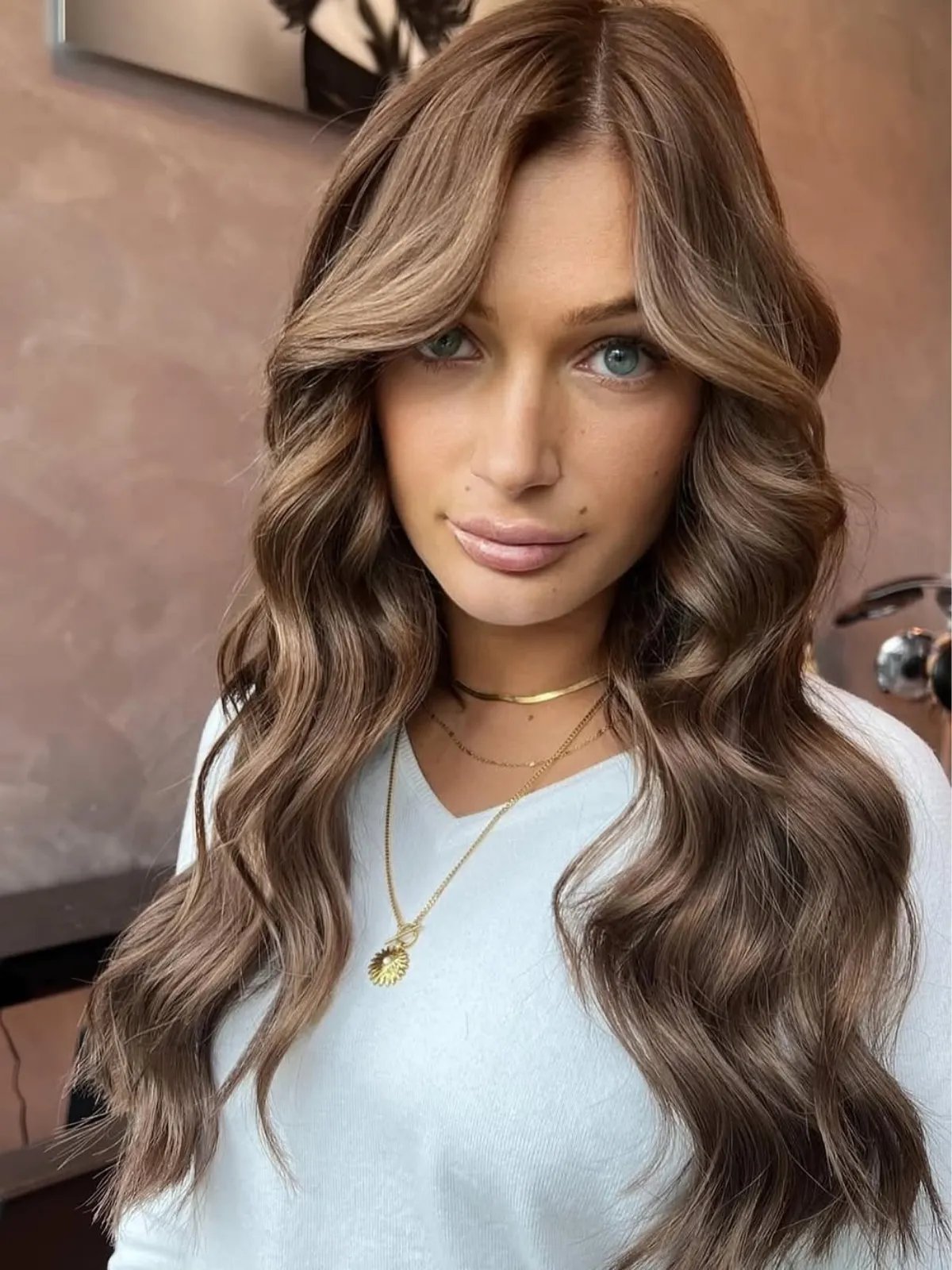 Model with a dark blonde reverse balayage, featuring golden tones through chocolate brown lengths.