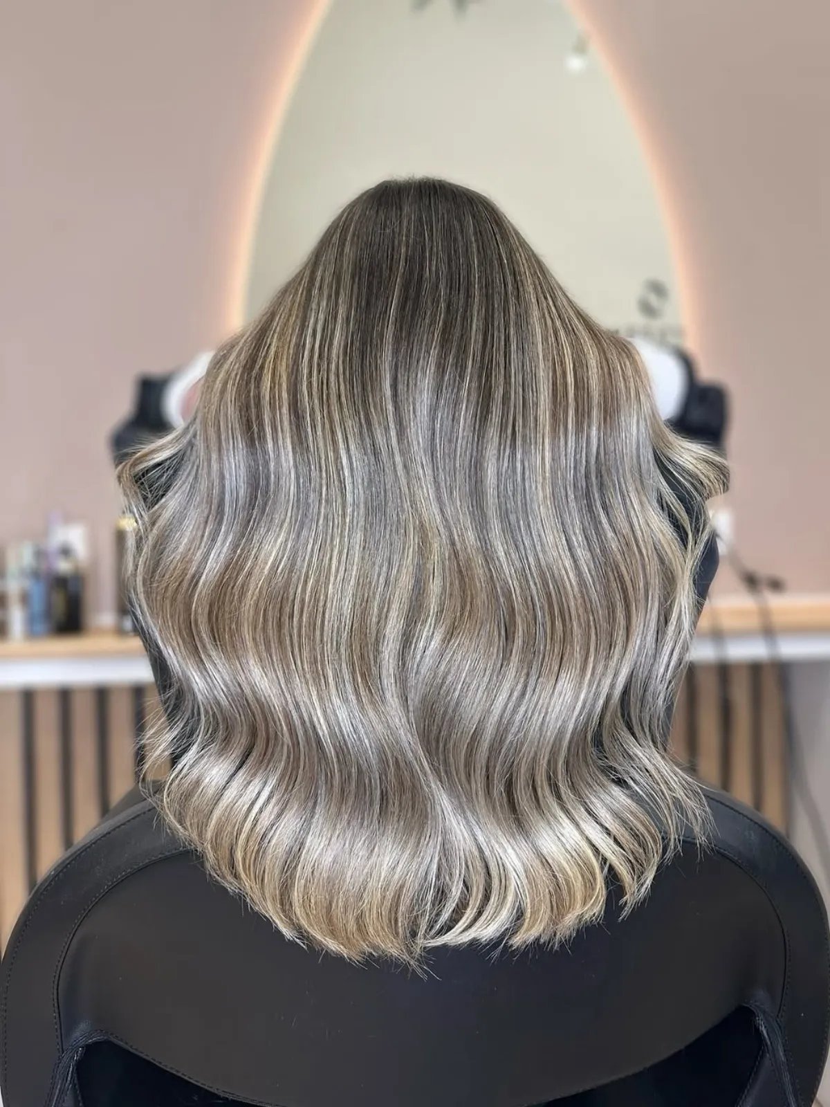 Back of model’s head showing dark hair roots with ash blonde lengths and ends.