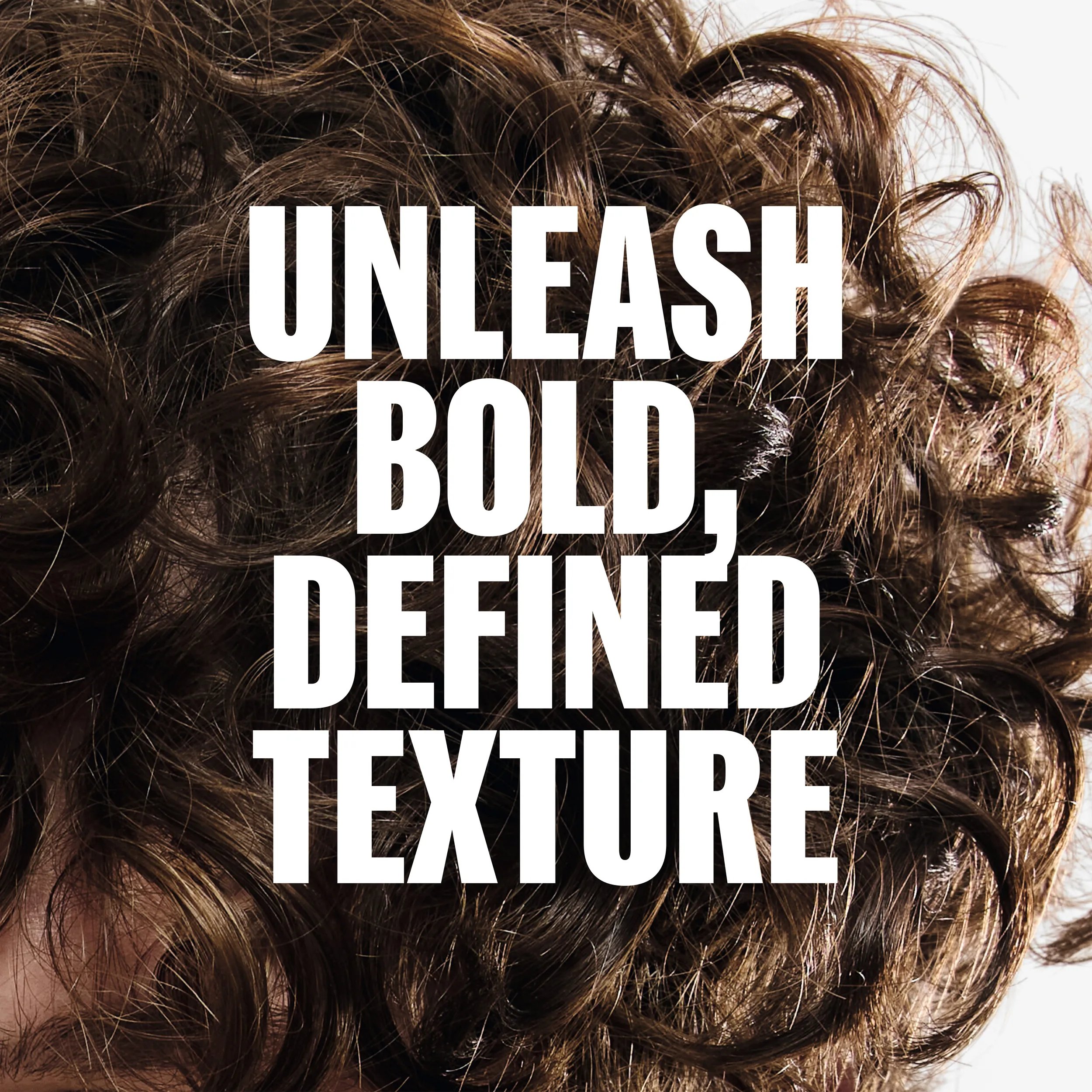 Primer plano de un cabello castaño, rizado y con textura, con el texto superpuesto en blanco: "DESATA UNA TEXTURA DEFINIDA Y ATREVIDA".