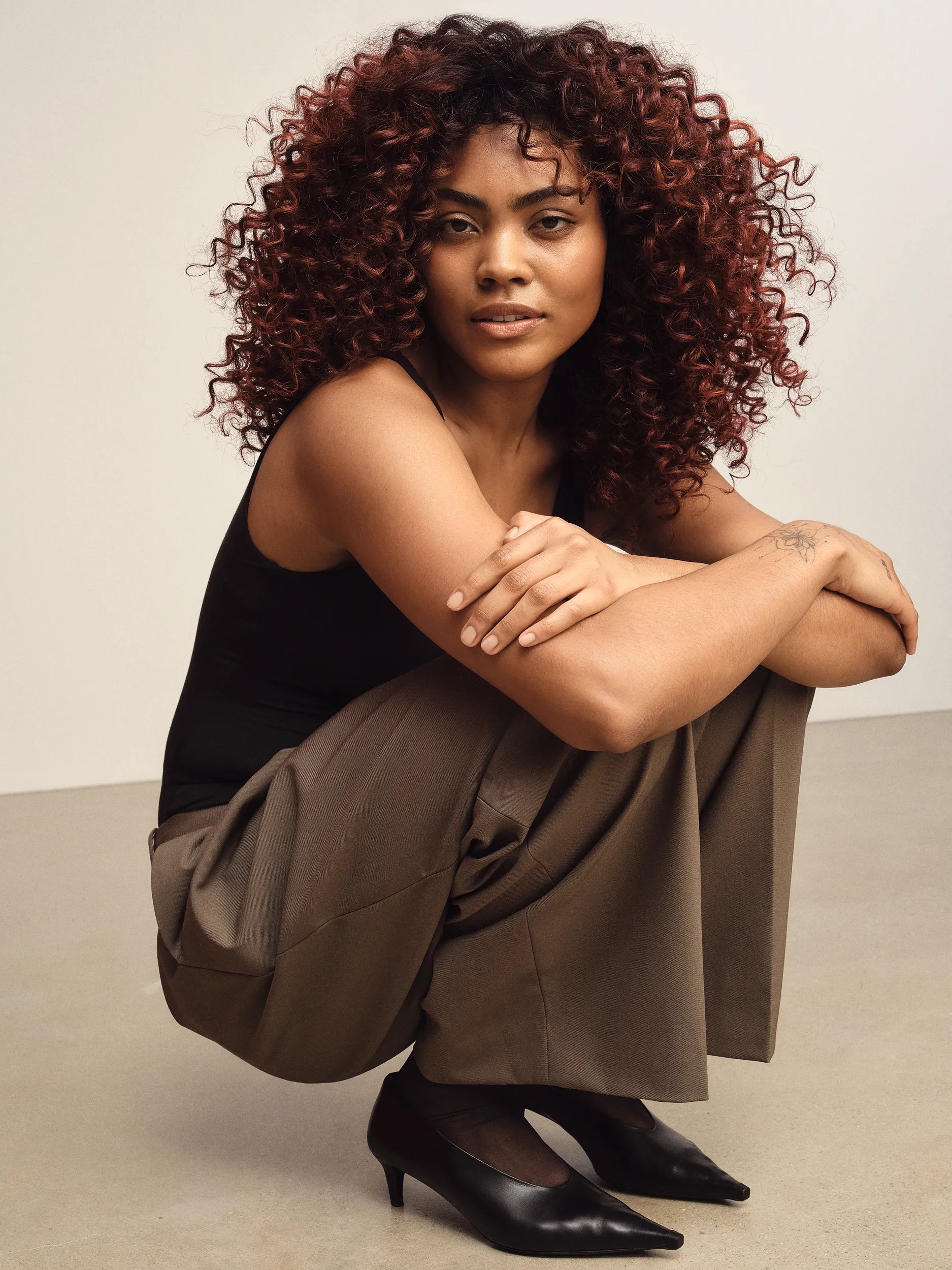 Image of woman with textured afro hair, wearing a black top against a white  wall