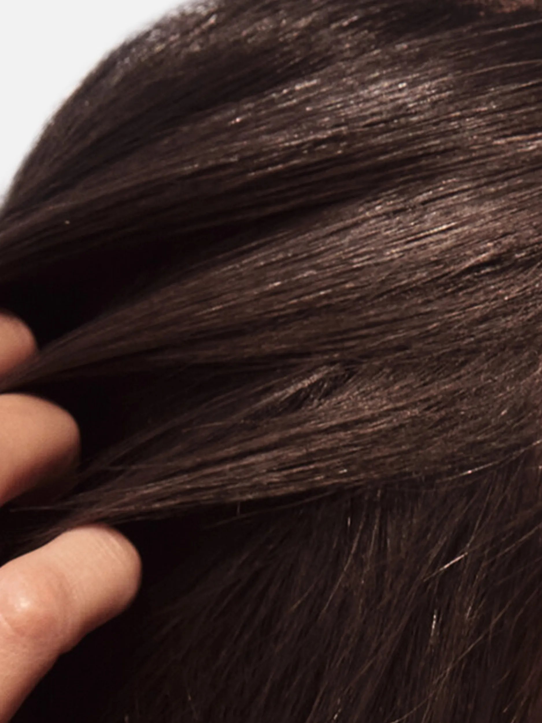 Close-up shot of dark brown, straight hair being lightly touched by a hand.