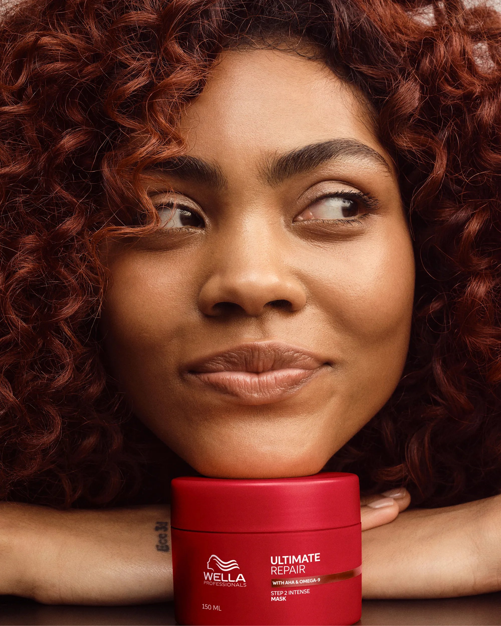 Model with curly hair holds up ULTIMATE REPAIR Mask.