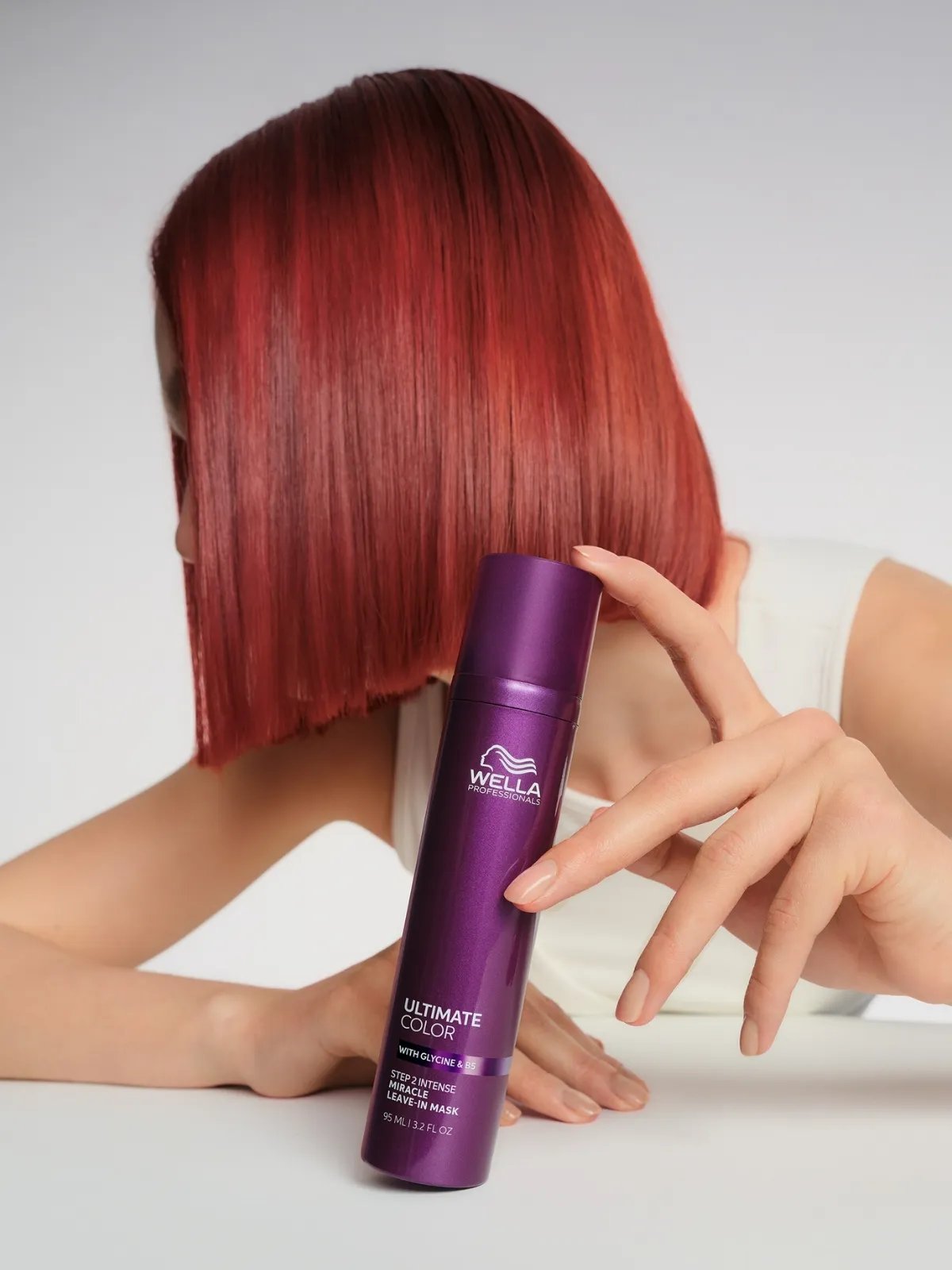 A red-haired model rests their hand on ULTIMATE COLOR Intense Miracle Leave-In Mask.