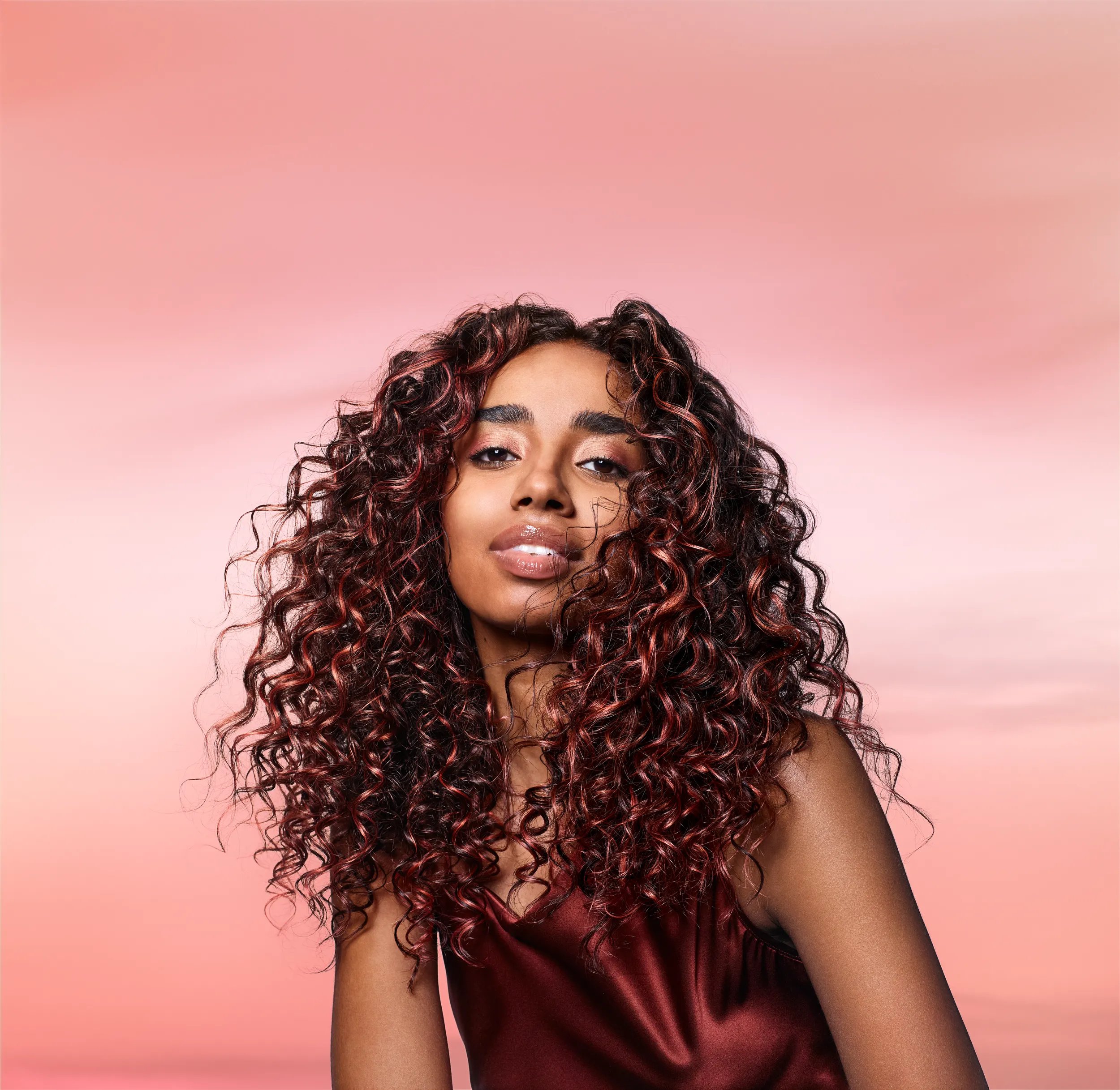 Model with long, dark, glossy, curly hair featuring coral highlights.