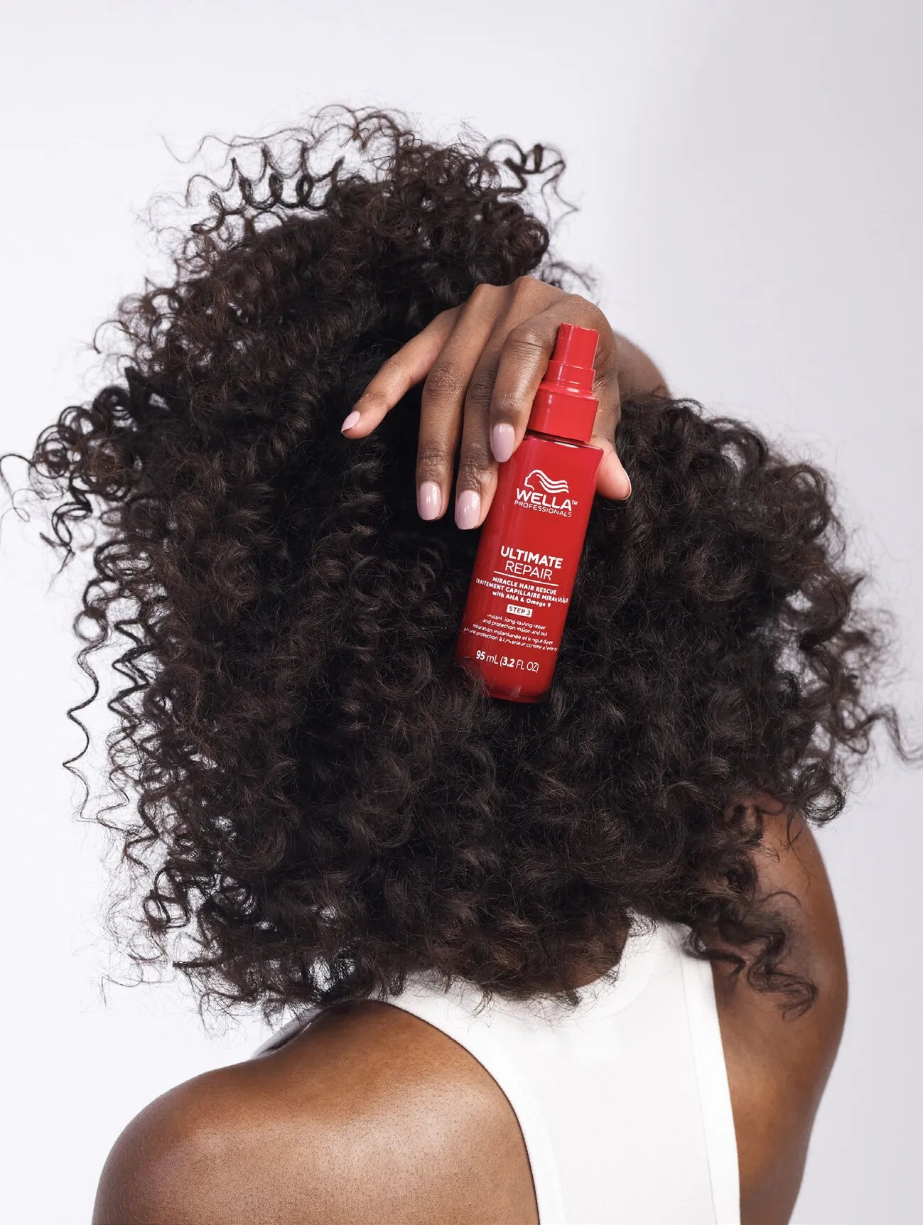 A model with brown, curly hair holds up a bottle of ULTIMATE REPAIR Miracle Hair Rescue.