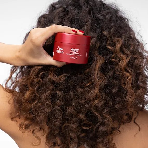 Back of model’s head with long, dark brown, curly hair. They’re holding up
the ULTIMATE REPAIR Mask.