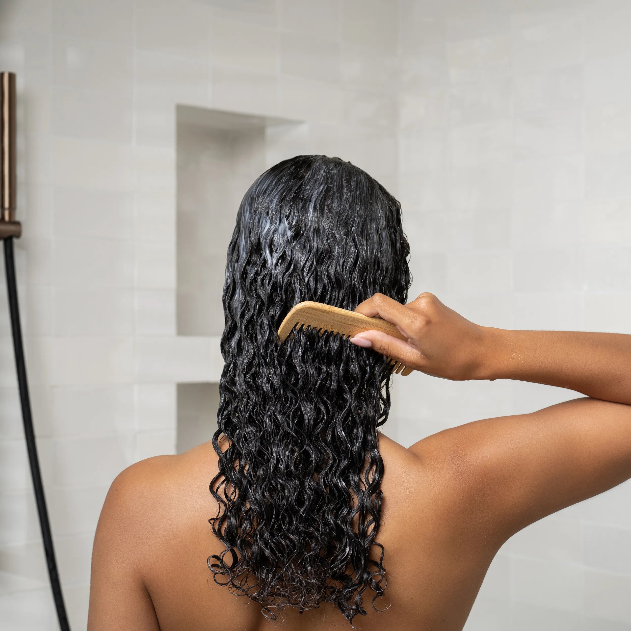 Model combs a hair treatment through wet, curly hair.