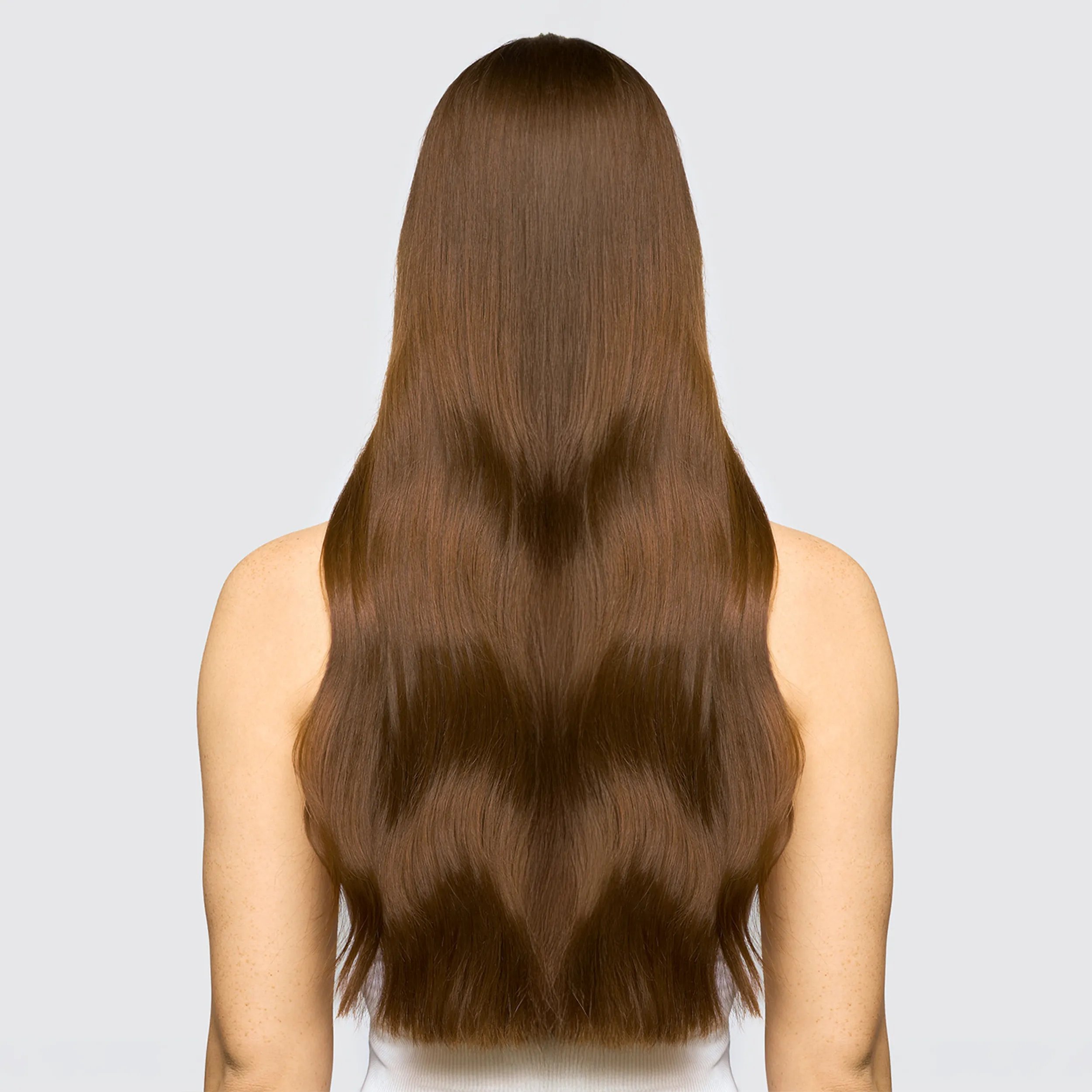 Model with long brown hair faces away from the camera. Hair is shiny and looks healthy after using Wella Professionals Ultimate Smooth products.