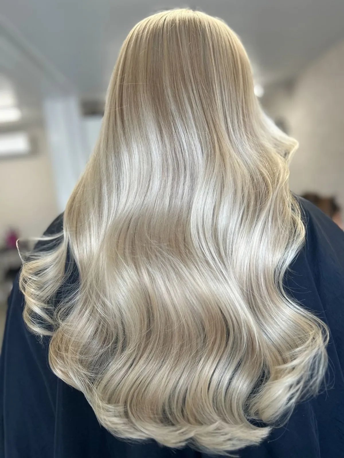 Back of model’s head with long, loosely curled, pearl blonde hair featuring dimensional highlights.