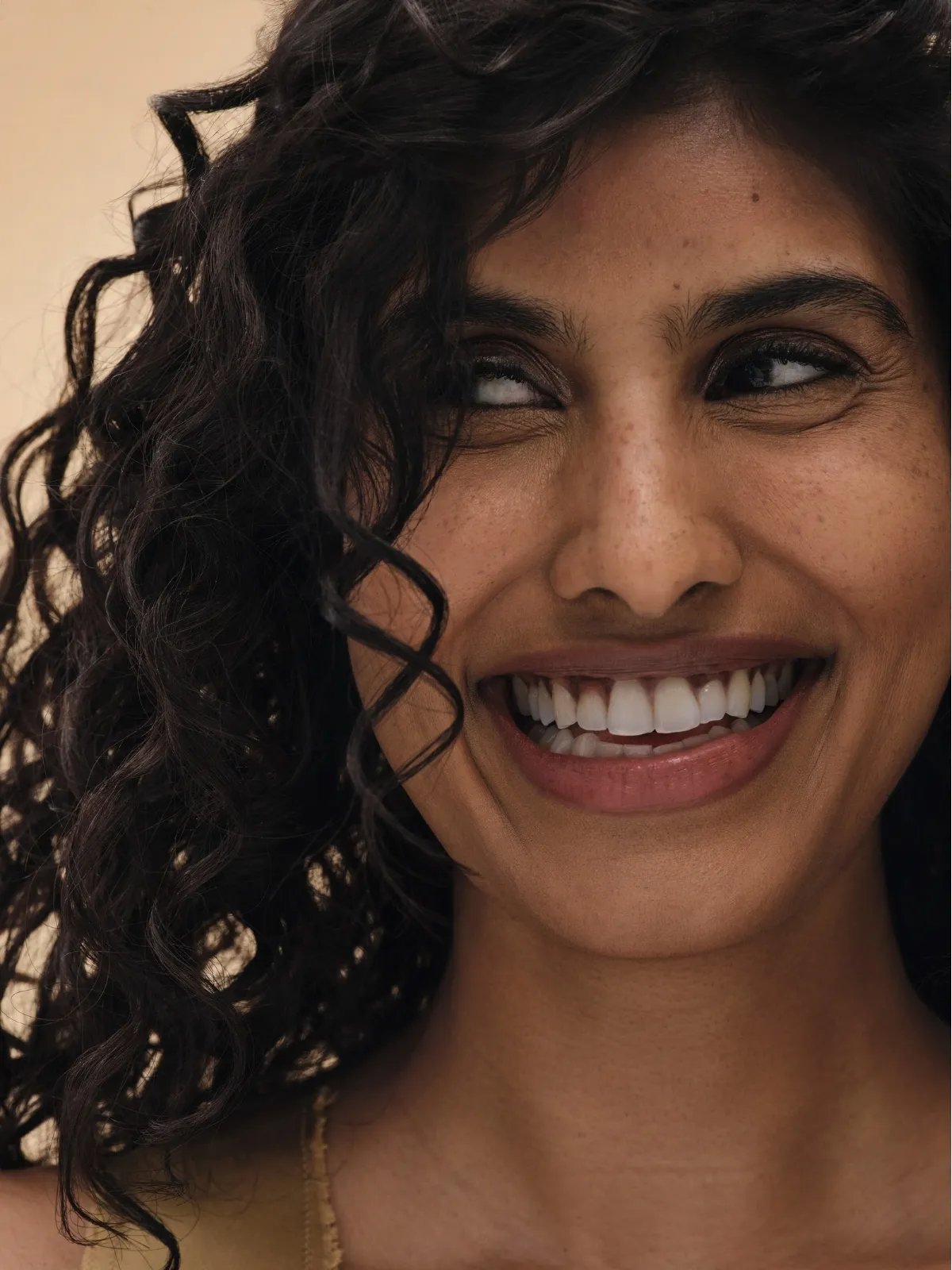 Model with frizz-free curls smiles while glancing sideways.