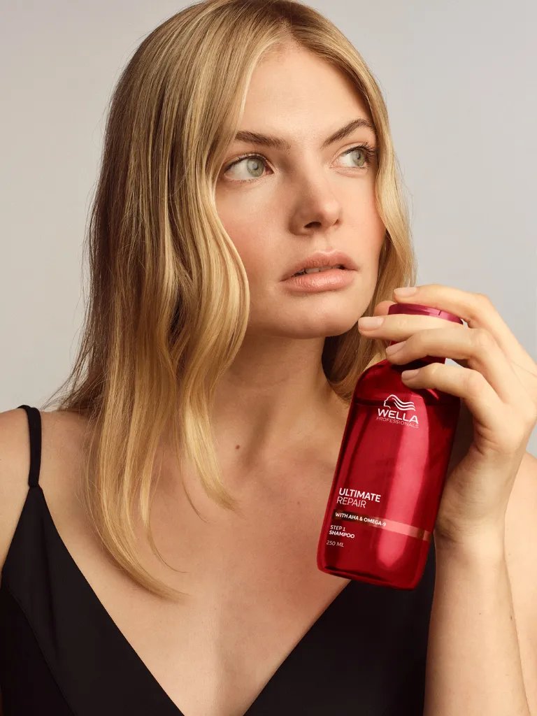 Blonde model holds a bottle of ULTIMATE REPAIR Shampoo.