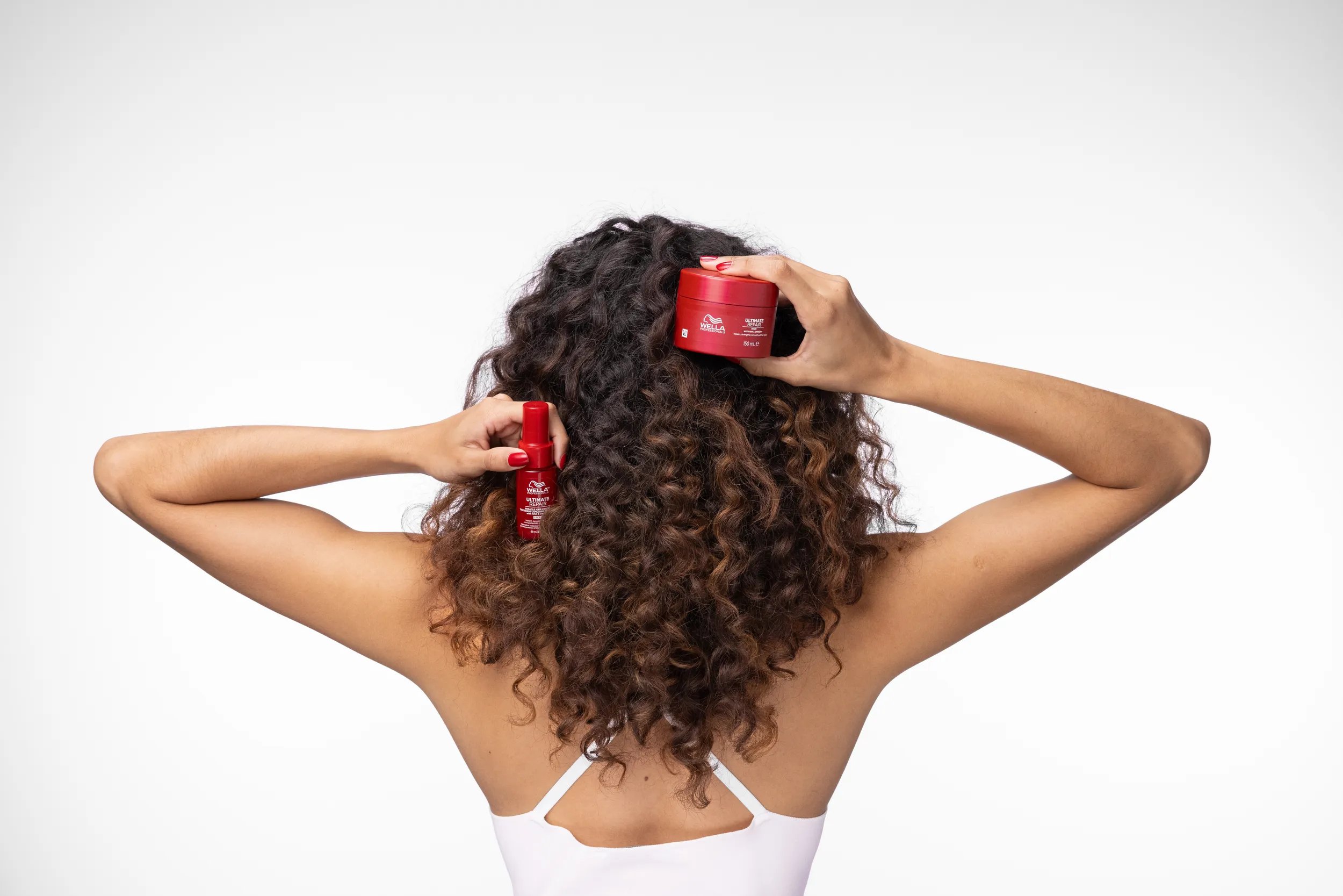 Model with curly hair holds up ULTIMATE REPAIR Miracle Hair Rescue and Mask.