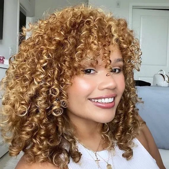 Model with honey blonde highlights through curly hair smiles at the
camera.