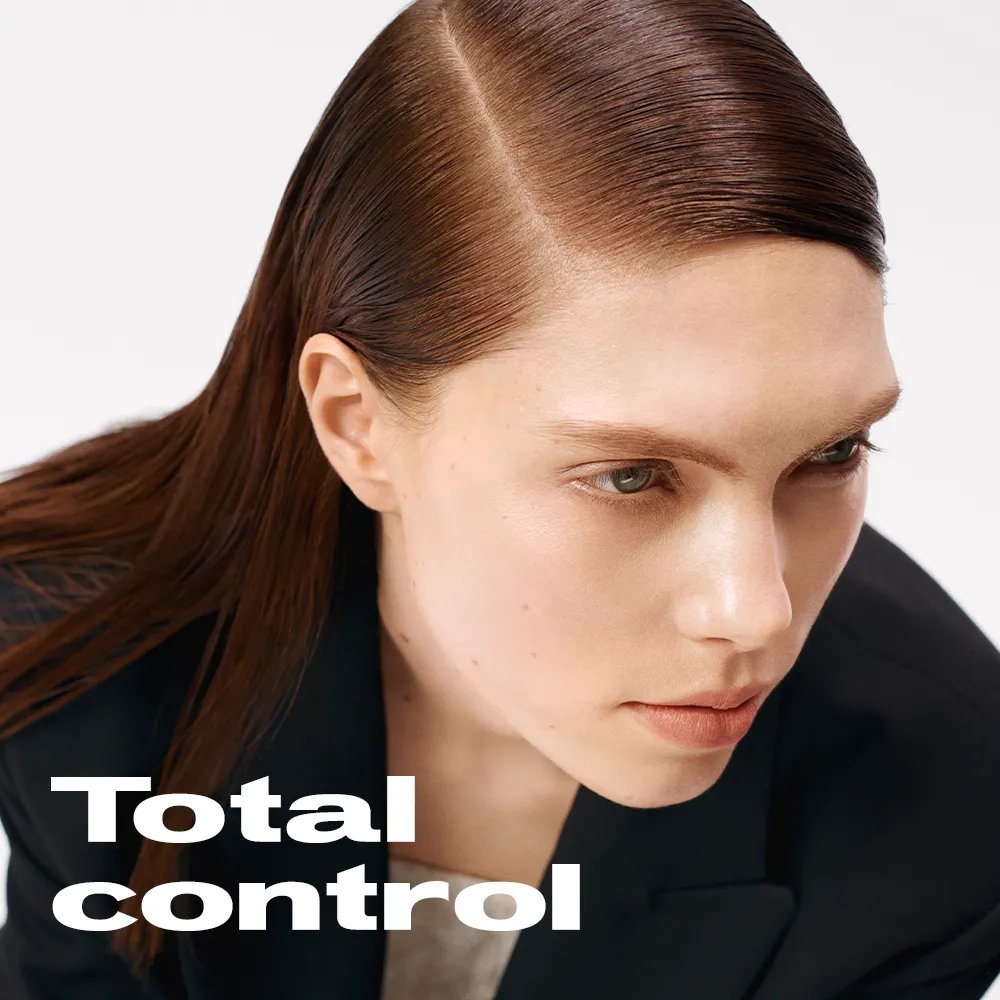 Aerial view of model with slicked red hair, wearing a black blazer, against a white background. Text overlaye reads "Total control" 
