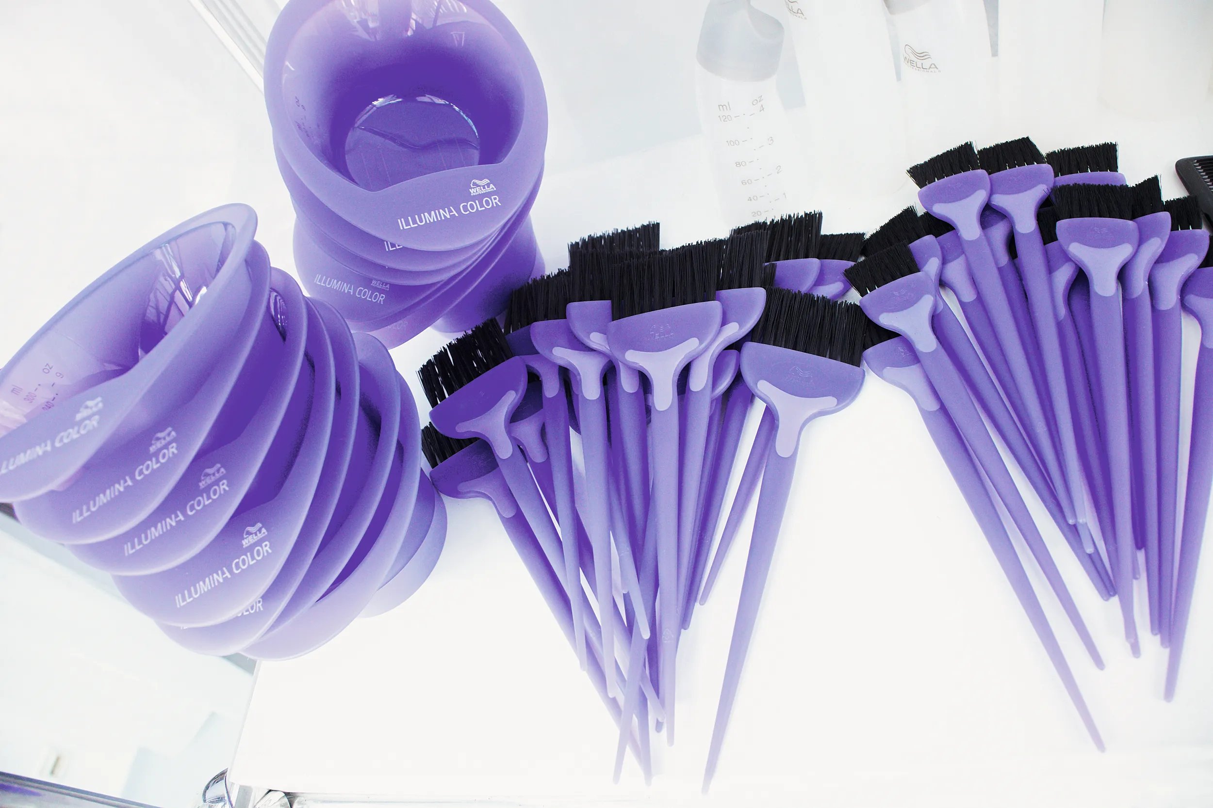 A set of purple hair coloring bowls and brushes branded with Illumina Color, neatly arranged on a white surface.