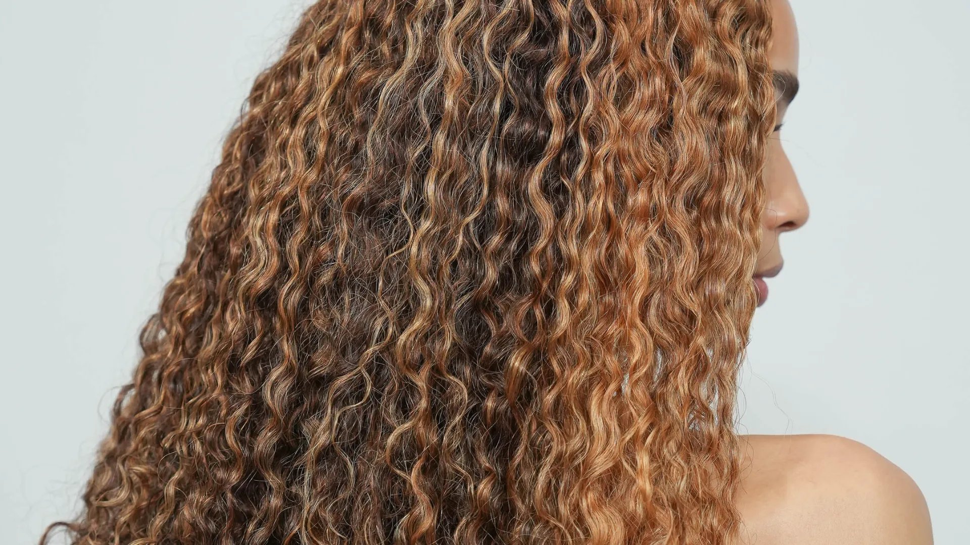 Model with dark brown, curly hair featuring caramel blonde highlights.