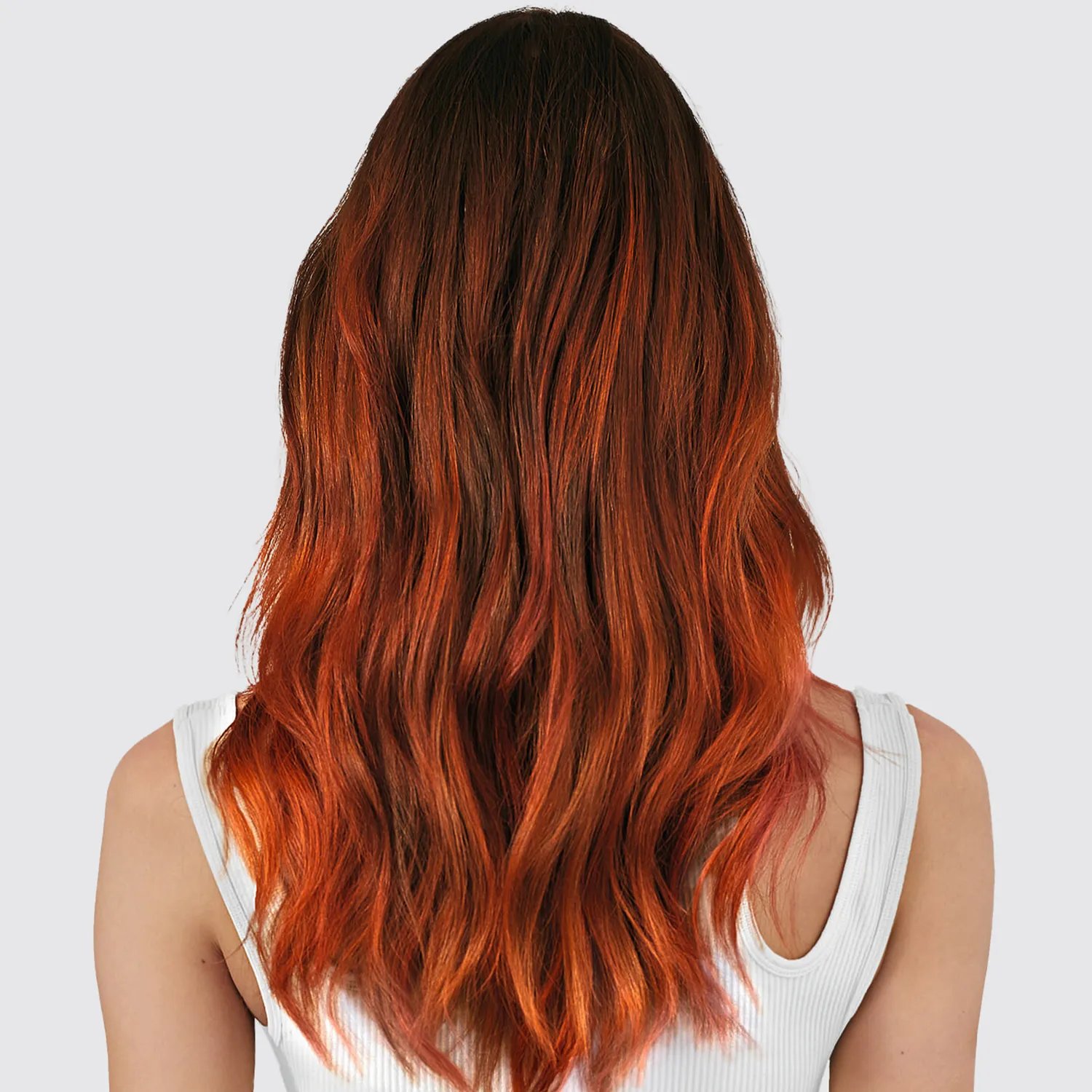 A female model with frizzy long hair. The color is darker red at the top graduating down to bright red ends, photographed from behind.