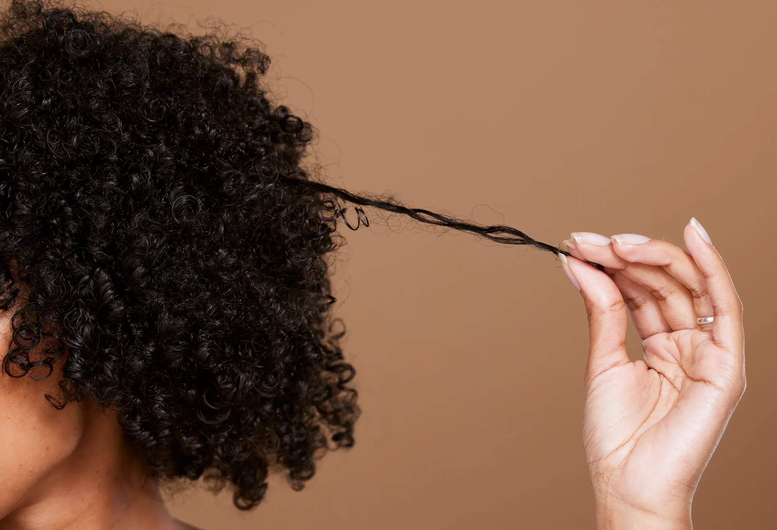 black woman with curly hair strengthening a strand of hair against brown background