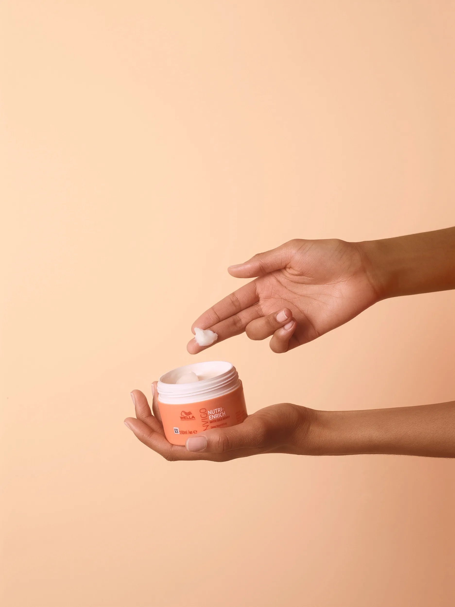 Hand taking some formula of Invigo Nutri-Enrich Mask over a orange background