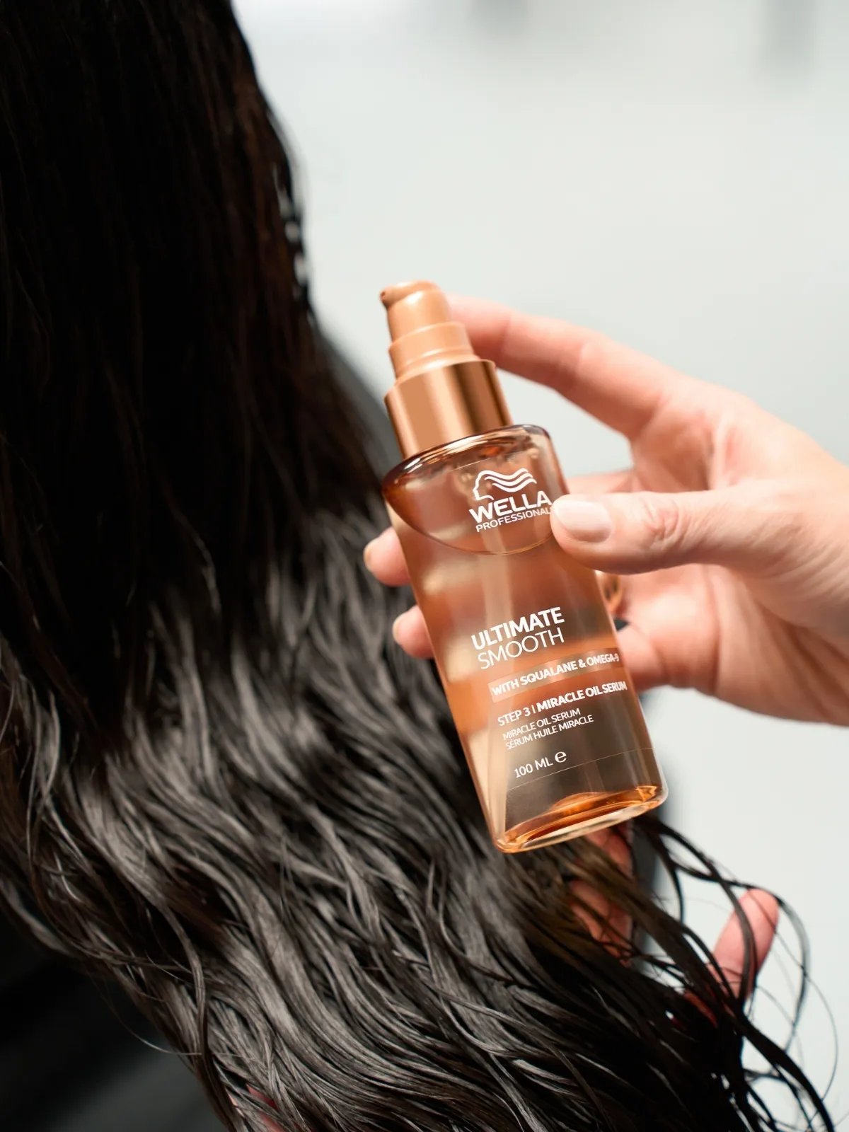 ULTIMATE SMOOTH Miracle Oil Serum is applied to model’s long, dark, damp hair.