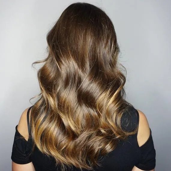 Model with long, wavy hair and dark blonde balayage, created using Wella Professionals. 