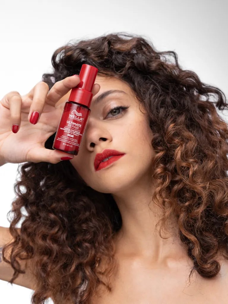 Model with dark brown, curly hair holds ULTIMATE REPAIR Miracle Hair Rescue. 