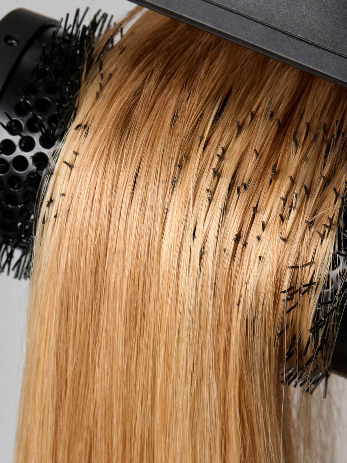 Round brush runs through a model’s blonde hair.