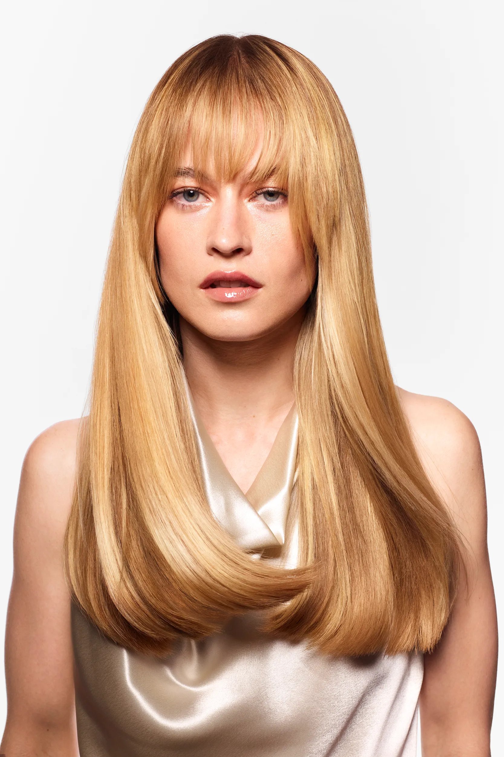 Model with long, golden hair that's dareker at the roots stares into the camera. Hair looks shiny and healthy.