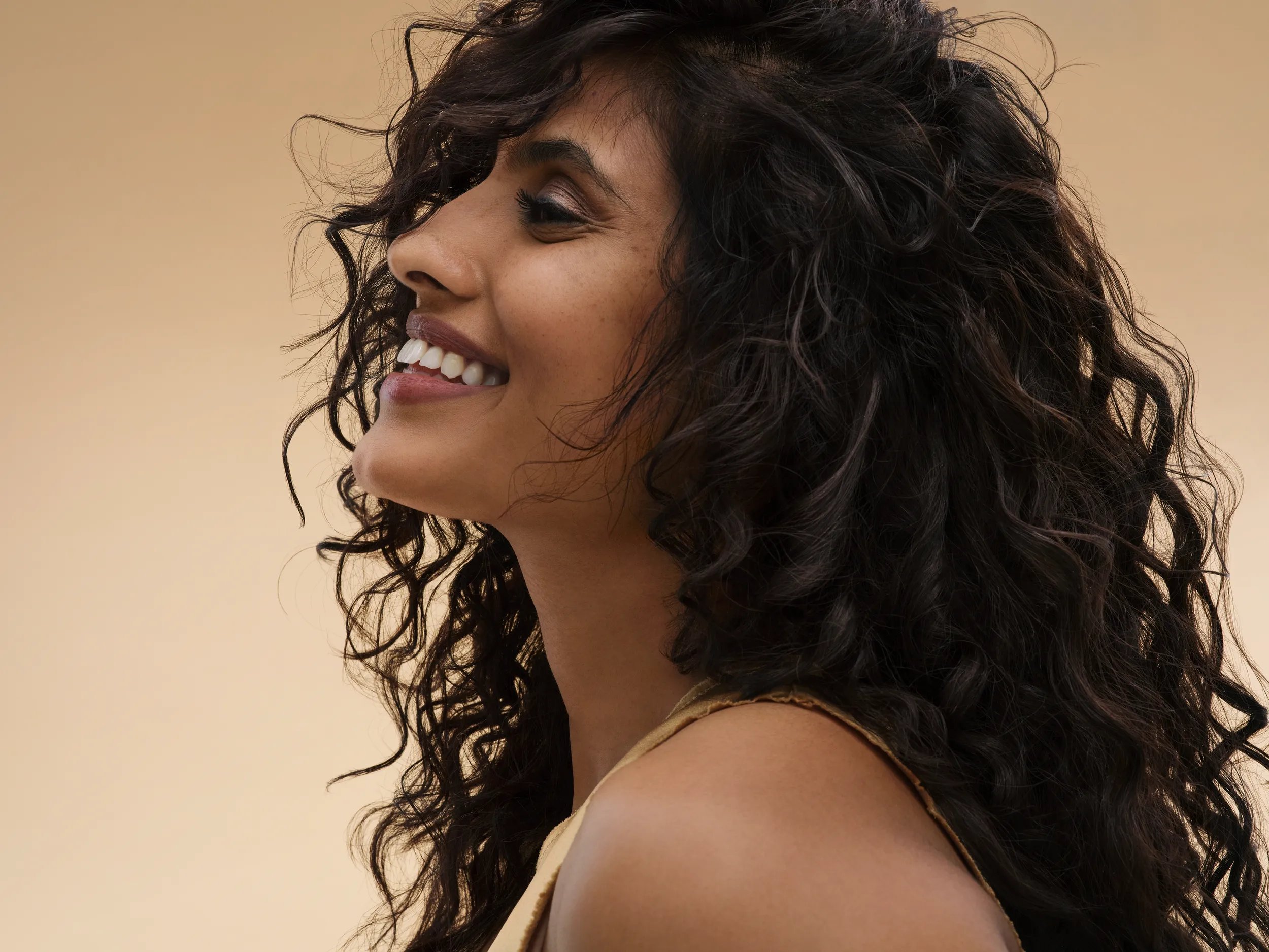 woman with voluminous, curly brown hair against a warm-toned background.