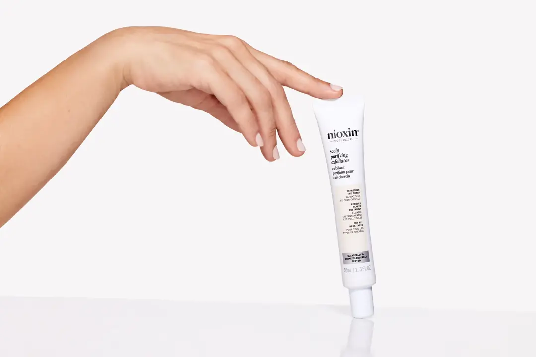 finger balancing Nioxin Scalp Purifying Exfoliator on white surface against white background