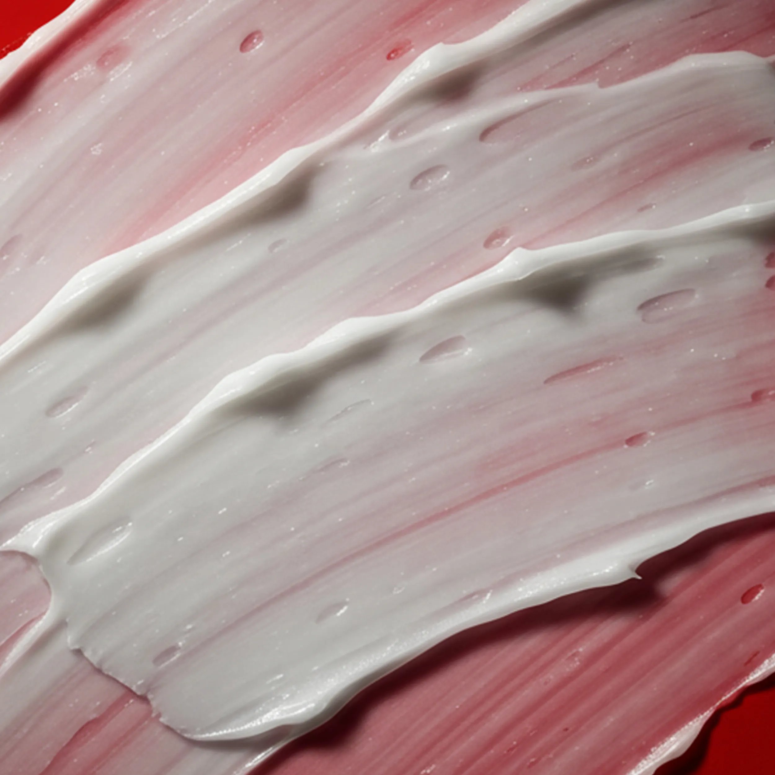Close up of a smear of cream against red background.
