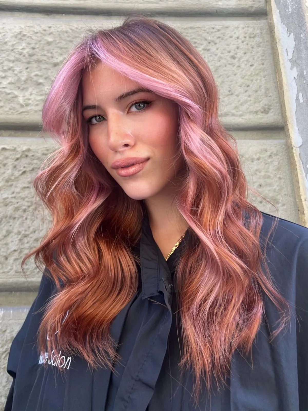 Model with long, wavy, rose gold hair featuring pastel pink face-framing highlights. 