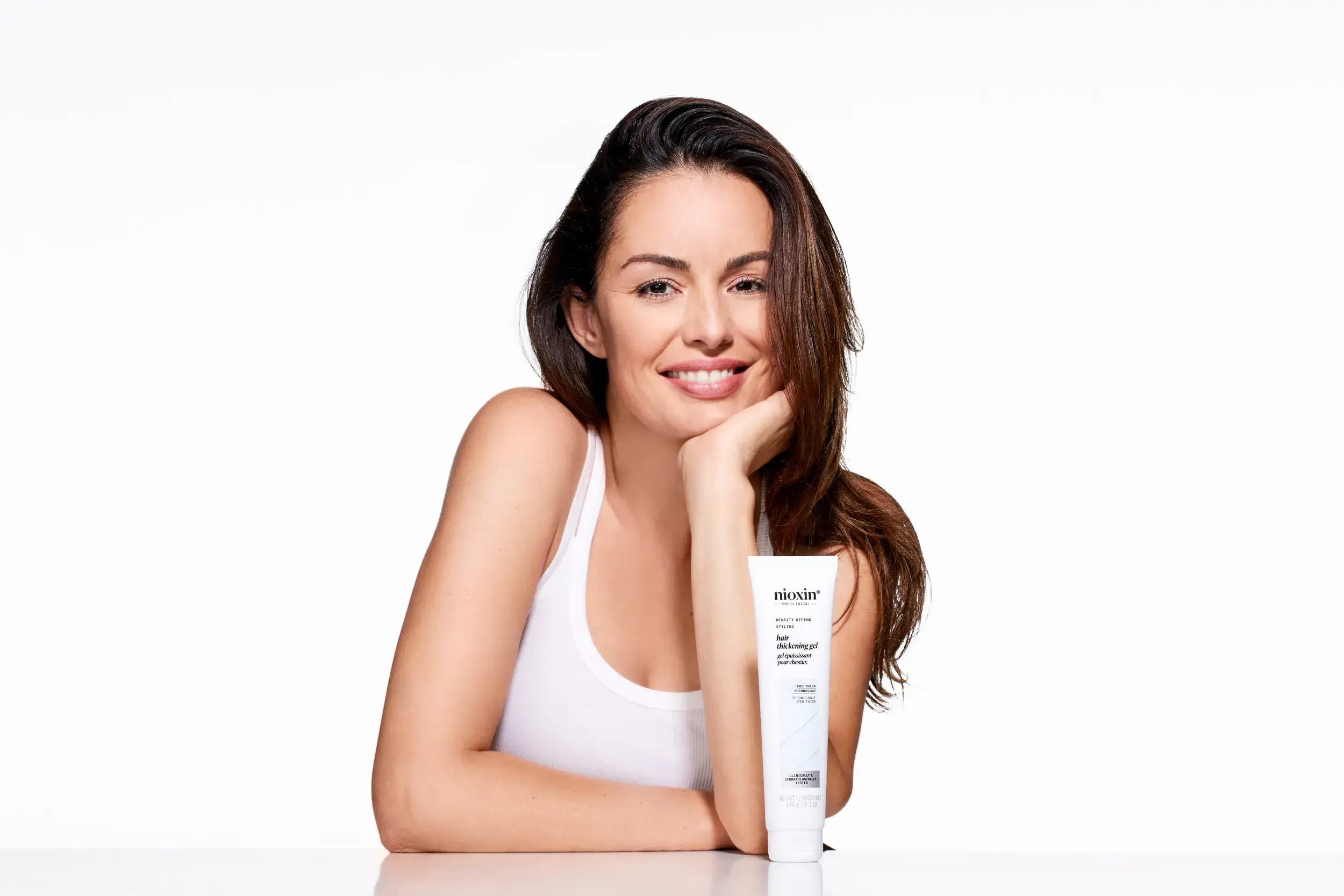 woman smiling with face resting in her palm and Nioxin thickening gel bottle on table in front of her