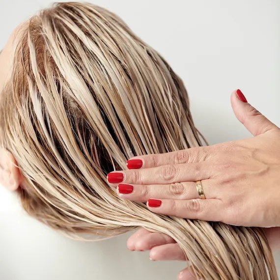 A close-up of a person’s wet blonde hair being held by a hand with red-painted nails.