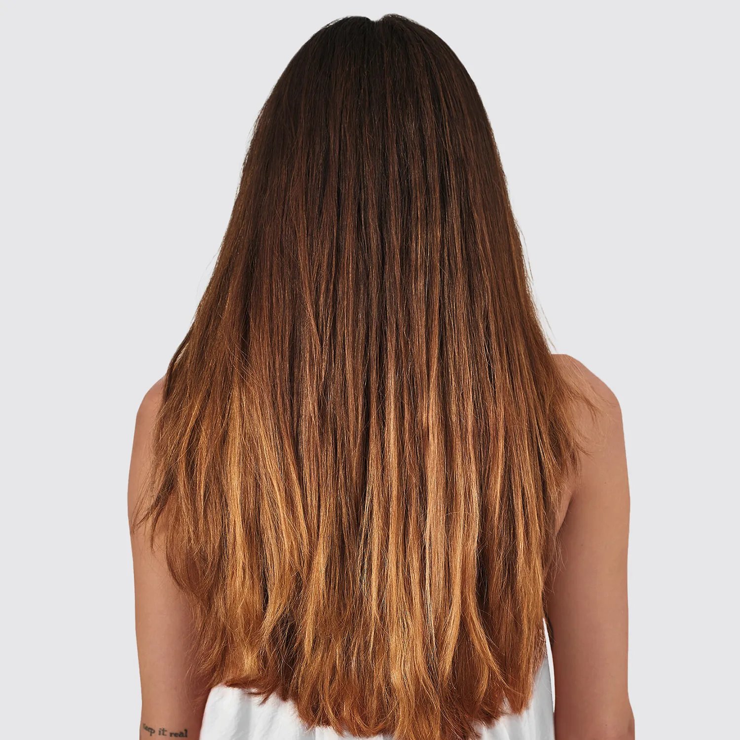 A female model with long hair, which is darker brunette at the top graduating down to copper at the ends, photographed from behind.