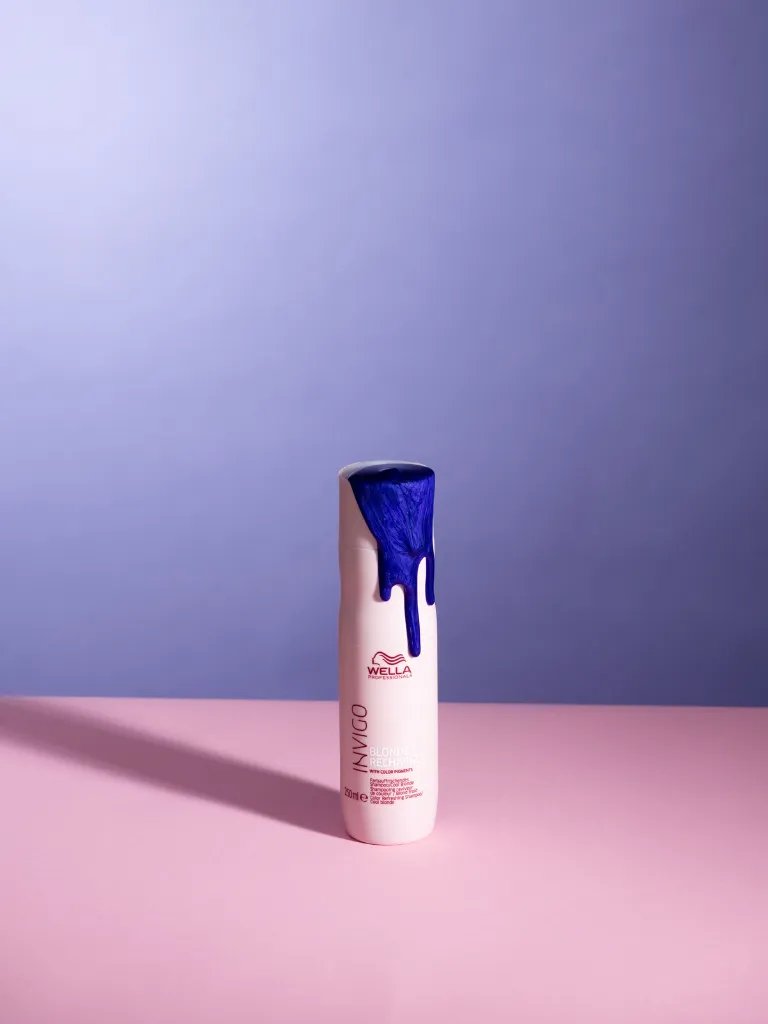 Purple shampoo spills over the side of a bottle of INVIGO Blonde Recharge Cool Blonde Shampoo.