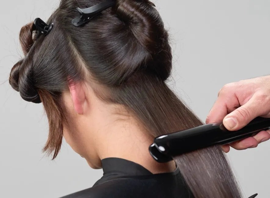 A close-up of a flat iron straightening blonde hair